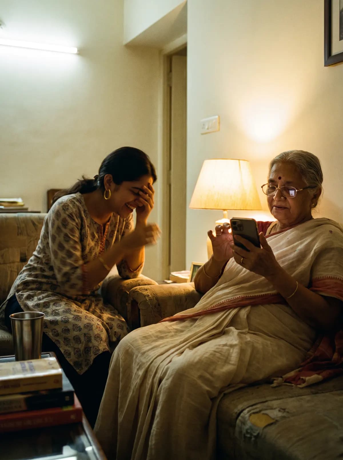 A grandmother types on a phone with one careful finger while her granddaughter laughs into her hands