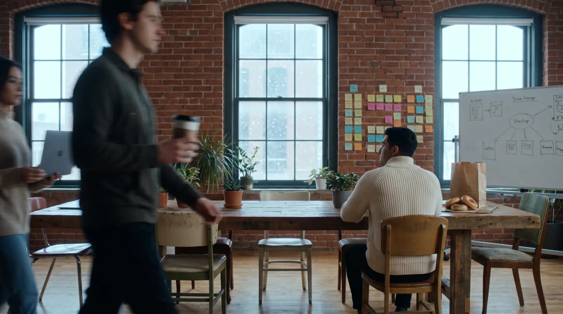 A small team in a Toronto loft on a snowy morning, two people blurred as they walk past, one sitting still at a long table
