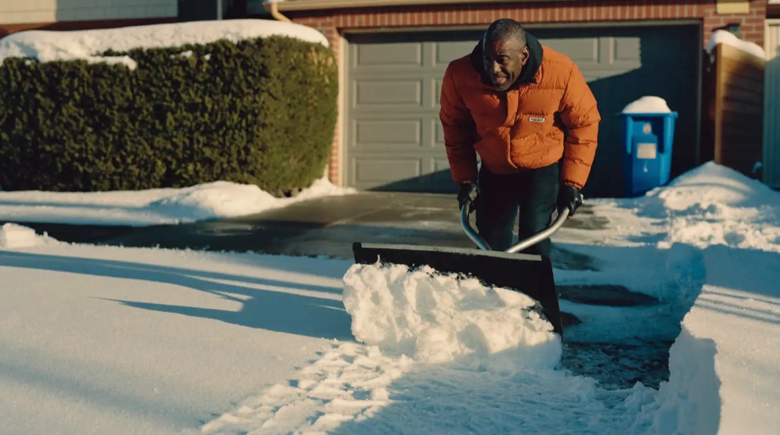 A snow pusher clearing a bare strip down a suburban Ontario driveway after a fall.