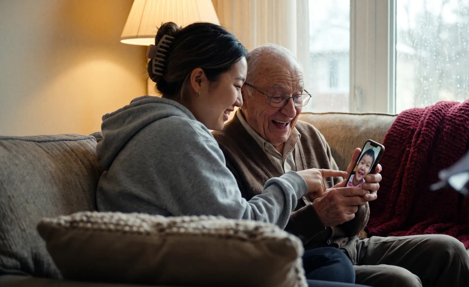 A student tutor points at a new smartphone as an elderly father makes his first video call to his grandchild, beaming
