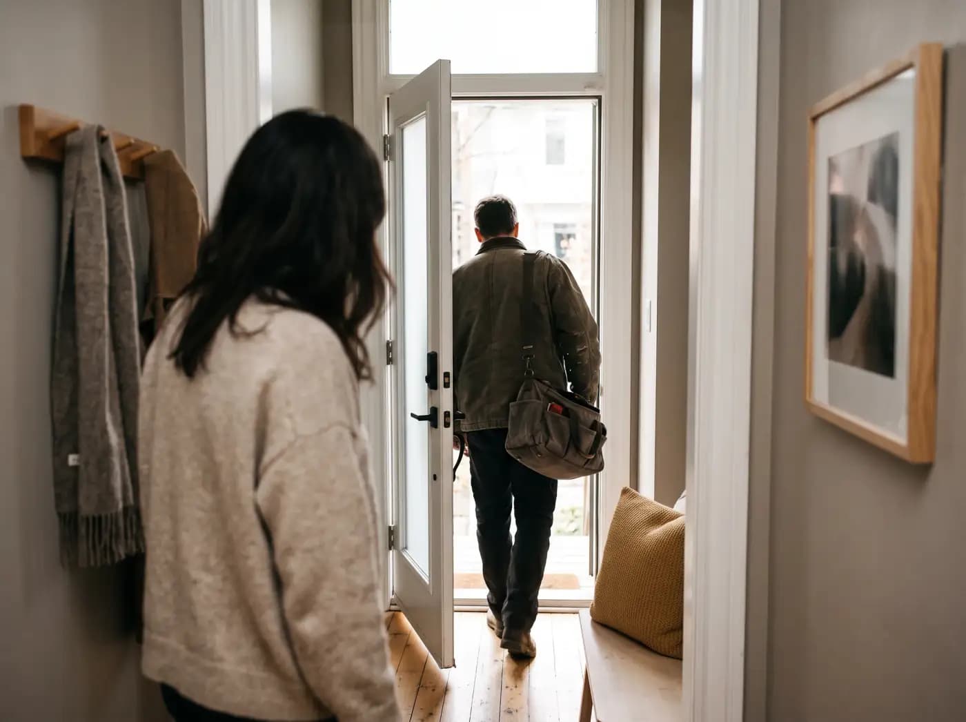 A homeowner opening their front door to a tradesperson carrying a tool bag