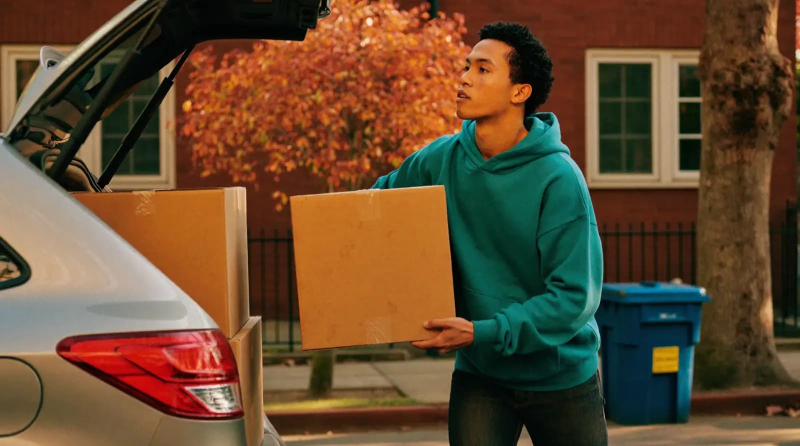 Boxes being loaded into the back of a hatchback on a residential street.